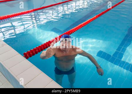 Ein glücklicher alter Mann steht im Urlaub in einem Pool mit sauberem Wasser an der frischen Luft. Stockfoto