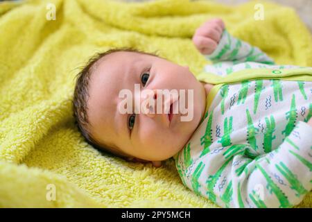 Ein wunderschönes, neugeborenes, weißes Baby liegt auf einer gelben Decke Stockfoto