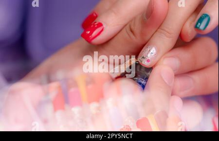 Eine Frau, die Fingernagel-Maniküre im Nagelsalon bekommt. Kosmetikerin malte Nägel im Nagel- und Wellnesssalon. Im Nagelstudio mit dem Schwerpunkt auf weißem und glitzerndem Nagellack und dem verschwommenen Vordergrund von gefälschten Nägeln. Stockfoto