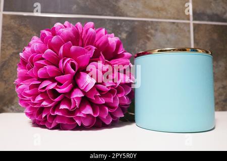 Dekorelemente im Badezimmer. Ein blaues Glas mit Badesahne oder Badesalz und eine rosa künstliche Doppelblume auf einem Regal. Schwarze Wandfliesen. Bad und WC-Innenausstattung. Stockfoto