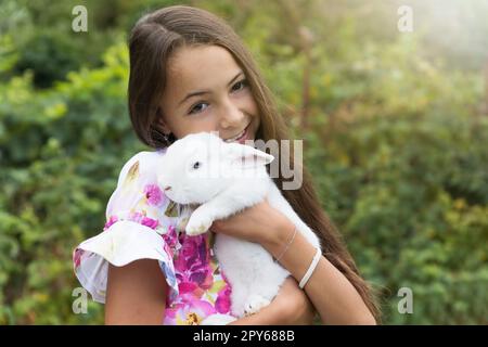 Das kleine Mädchen hält ein weißes Kaninchen in den Armen. Stockfoto