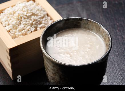 Amazake vor schwarzem Hintergrund und Reis-Koji in einer Masu-Box. Stockfoto