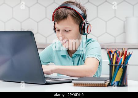 Porträt eines jungen Kindes, der Kopfhörer trägt, vor dem Laptop sitzt, tippt, chattet, Nachrichten sendet, kommuniziert. Stockfoto