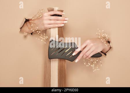 Hände mit Blumen halten Haarsträhnen für Verlängerungen auf beigefarbenem Hintergrund. Stockfoto