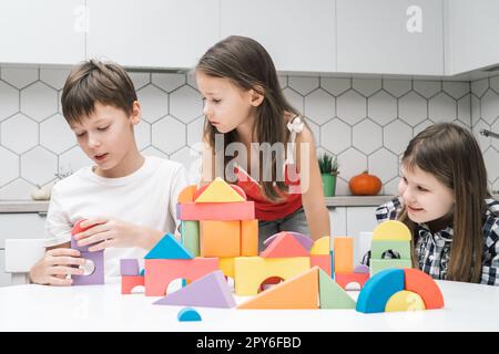 Kleine Freunde spielen Baumeister auf dem Tisch. Mädchen sehen sich den Jungen an und sammeln farbenfrohe Details von lego. Kinder bauen eine Spielzeugstadt. Stockfoto