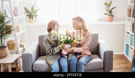 Mutter und Tochter sitzen auf dem Sofa mit Tulpen in der Hand. Stockfoto