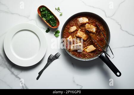 Bratpfanne mit indischem Lachs-Curry. Gebratene Lachsfilets, in Currysauce auf der Grundlage roter Tomaten und anderer Gemüse. Leeres, sauberes Weiß Stockfoto