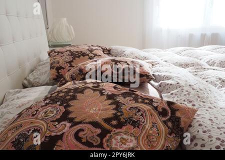 Pinke dekorative Kissen auf der Bettwäsche. Doppel-Hochzeitsbett mit Kissen und dicker Federdecke. Schlafzimmerdesign. Weiches weißes Kopfteil. Einrichtung mit Möbeln und Bettwäsche. Stockfoto