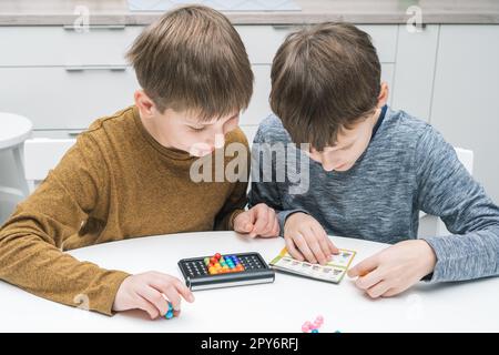 Glückliche Schuljungen spielen Spielzeugbauer am Tisch. Kinder lesen Spielregeln. Sammle Details auf dem Spielbrett aus Plastik. Stockfoto