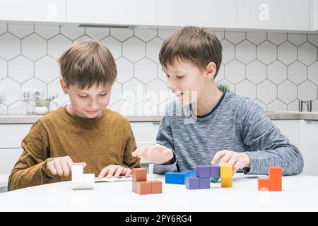 Glückliche Schuljungen spielen Spielzeugbauer am Tisch. Kinder sammeln farbige Details von lego und falten Tetris-Figuren. Stockfoto