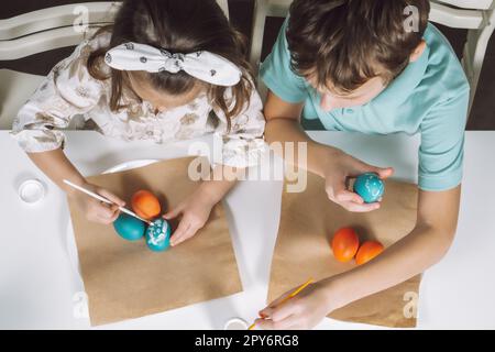 Porträt zwei Kinder, kleines Mädchen, Geschwister, mehrfarbige Ostereier in der Küche, Pinsel. Draufsicht Stockfoto