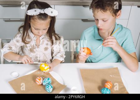 Porträt zwei Kinder, kleines Mädchen, Geschwister, mehrfarbige Ostereier in der Küche, Pinsel. Draufsicht Stockfoto