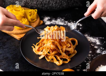 Eine Nahaufnahme von Händen, die eine Gabel halten und in einem Teller mit Fast Food in einer Küche graben. Stockfoto