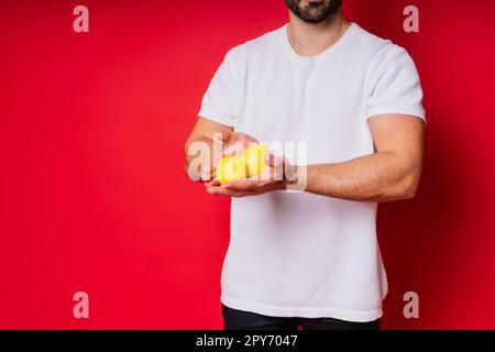 Porträt eines jungen bärtigen Mannes, der Zitronen in beiden Händen auf einem isolierten roten Hintergrund hält Stockfoto