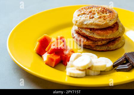 Pfannkuchen auf einem gelben Teller mit Obst und Schokolade. Stockfoto