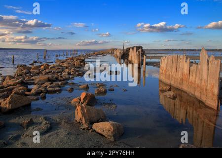 Das Foto wurde in der Ukraine in der Nähe der Stadt Odessa aufgenommen. Das Bild zeigt einen alten, zerstörten Pier auf einer salzigen Flussmündung namens Kuyalnik. Wolken sind in sichtbar Stockfoto