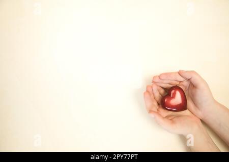 Frau mit rotem Herz in den Händen auf hellem farbigem Hintergrund, Kopierbereich von oben, Liebe, Romantik, Muttertag, Valentinstag, weiche Farbfamilie Stockfoto