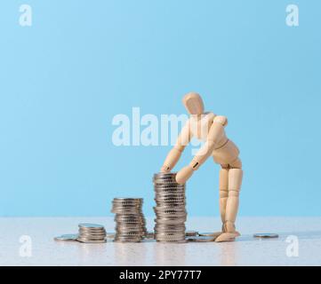 Eine Schaufensterpuppe aus Holz und ein Münzstapel auf blauem Hintergrund Stockfoto