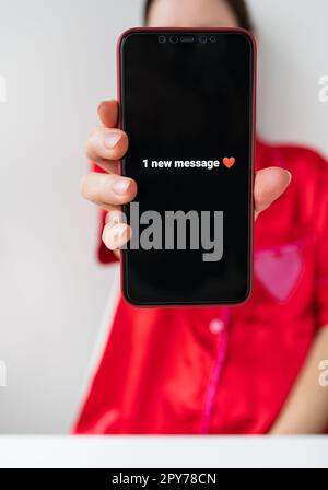 Glückliches Mädchen hält ein Smartphone mit einem aktivierten Bildschirm mit 1-Textnachricht in Form eines Herzens, Nahaufnahme des Smartphones. Februar 14 Valentinstagskonzept. Stockfoto