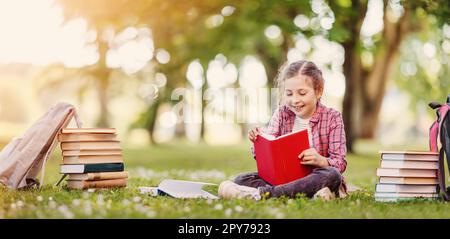 Einsamkeitsmädchen sitzt auf der grünen Wiese und liest ein Buch. Stockfoto