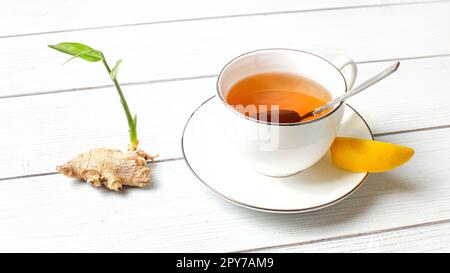 Porzellan Tasse mit heißem Tee, Bernstein und Scheibe der Zitrone, Ingwer Wurzel grün sprießen Text auf weißem boards Schreibtisch. Stockfoto