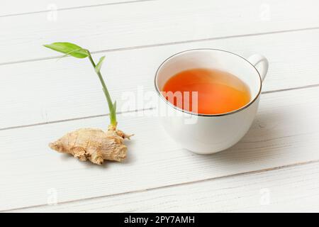 Weißes Porzellan Tasse mit heißem Tee gelb, chemische Ingwerwurzel und Grün neben es auf White boards Schreibtisch sprießen. Stockfoto