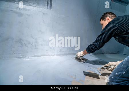 Verteilen Sie die Dämmung mit einer Kelle auf dem Betonboden Stockfoto