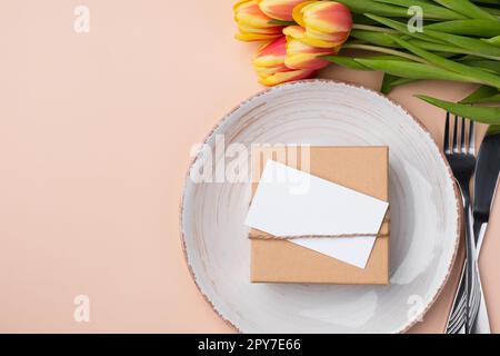 Modell mit festlichem Tischbezug, Tulpen und einem Geschenk auf beigefarbenem Hintergrund. Stockfoto