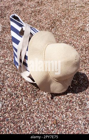 Strandzubehör Tasche und Sonnenhut auf Kieselstrand in der Nähe des Meeres. Sommerhintergrund. Stockfoto