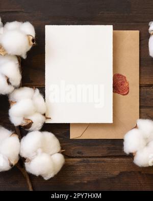 Unbeschriftete Karte und Umschlag mit Baumwollblumen Draufsicht auf dunkelbraunem Holz, Hochzeitsmodell Stockfoto