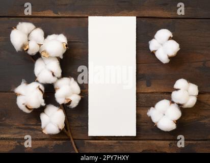 Unbeschriftete Karte mit Baumwollblumen Draufsicht auf dunkelbraunem Holz, Hochzeitsmodell Stockfoto