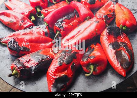 Rösten Sie köstliche rote Paprika für einen rauchigen Geschmack und schnelles Schälen. Balkansalatrezepte. Thermische Verarbeitung der Pfefferpflanze auf einem Metallkreis. Die Paprika werden auf einem flachen Backblech aufgemacht Stockfoto