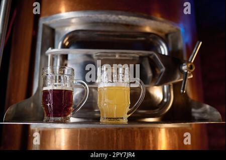 Frisch zubereitetes helles und dunkles Craft-Bier in einem Glasbecher, der auf einem Fass steht Stockfoto