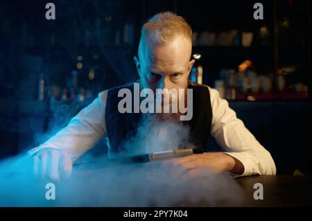 Das Porträt eines stilvollen bärtigen Mannes atmet Rauch aus, während er eine Wasserpfeife raucht Stockfoto