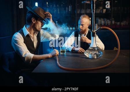 Stilvolle Gangster, die in der Bar eine Hookah rauchen und ein Geschäftstreffen abhalten Stockfoto