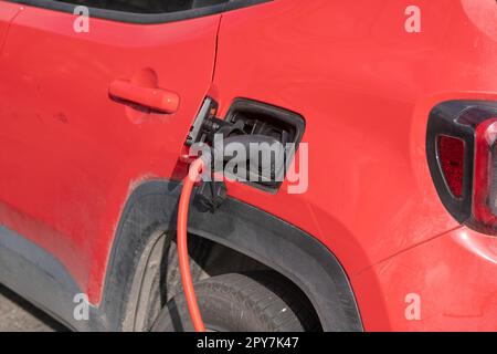 Das elektrische rote Auto wird aufgeladen, mit dem roten Kabel an die elektrische Einheit angeschlossen, wo es Energie verbraucht, dedizierte Parkplätze. Keine Emissionen in CIT Stockfoto