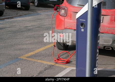 Das elektrische rote Auto wird aufgeladen, mit dem roten Kabel an die elektrische Einheit angeschlossen, wo es Energie verbraucht, dedizierte Parkplätze. Keine Emissionen in CIT Stockfoto