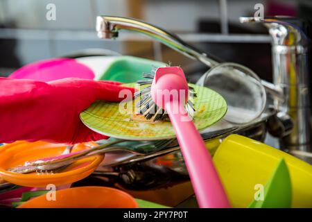 Das Waschbecken war voller schmutzigem Geschirr. Eine Frau in rosa Gummihandschuhen, die mit einem Pinsel abspült. Dunkle Arbeitsfläche in moderner Küche. Hausarbeiten Stockfoto