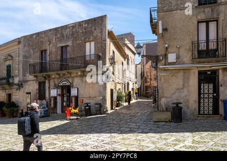 Ein Platz im Zentrum der mittelalterlichen Stadt Erice in Sizilien Italien mit seinen typischen quadratischen Kopfsteinpflastersteinen und mediterranen beigen Häusern in der Sonne. Stockfoto