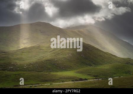 Doolough Valley, Glenummera und Glencullin Bergketten, die von Sonnenstrahlen erleuchtet werden, Irland Stockfoto