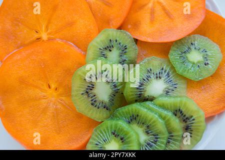 Frische reife saftig Kiwi Scheiben mit Persimmon auf einer Platte angeordnet, Ansicht von oben Stockfoto