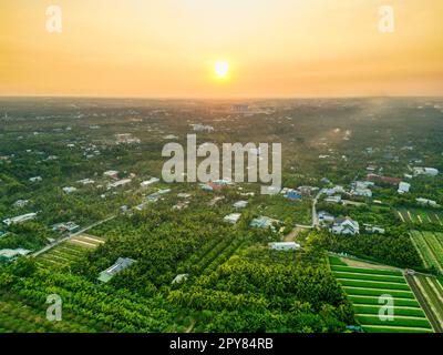 Golden Hour Magic: Atemberaubender Sonnenuntergang über den Feldern der Provinz Tien Giang mit dem ruhigen Fluss und der Stadtlandschaft in Vietnam Stockfoto