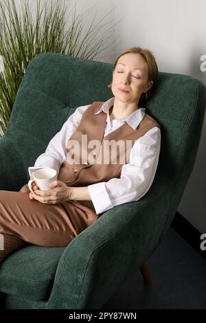 Eine Frau mittleren Alters, die sich während der Kaffeepause im Büroerholungsraum ausruht Stockfoto