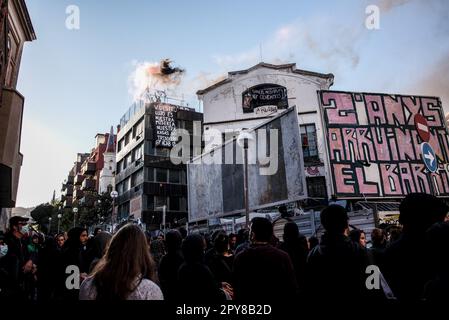 Barcelona, Spanien. 02. Mai 2023. Zwei Demonstranten halten während der antifaschistischen Kundgebung in Barcelona Lichtfackeln auf dem Dach eines Squats mit einem Schild, auf dem steht: "Ihr Luxus ist unser Elend, unsere Häuser sind Schützengräben". Etwa 250 Menschen aus der antifaschistischen Bewegung versammelten sich vor dem Squat „La Ruina“, um die Durchfahrt der Nachbarn und der Polizei zu verhindern. Etwa 50 Menschen wurden im Haus verbarrikadiert. Kredit: SOPA Images Limited/Alamy Live News Stockfoto