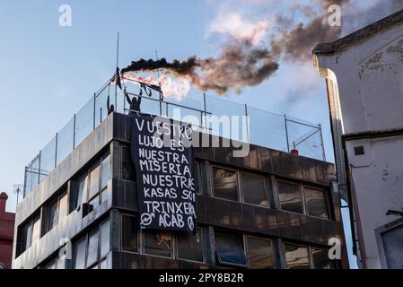 Barcelona, Spanien. 02. Mai 2023. Zwei Demonstranten halten während der antifaschistischen Kundgebung in Barcelona Lichtfackeln auf dem Dach eines Squats mit einem Schild, auf dem steht: "Ihr Luxus ist unser Elend, unsere Häuser sind Schützengräben". Etwa 250 Menschen aus der antifaschistischen Bewegung versammelten sich vor dem Squat „La Ruina“, um die Durchfahrt der Nachbarn und der Polizei zu verhindern. Etwa 50 Menschen wurden im Haus verbarrikadiert. Kredit: SOPA Images Limited/Alamy Live News Stockfoto