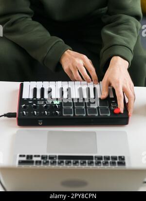 Mann, der elektronische Musiktitel mit tragbarer MIDI-Tastatur auf einem Laptop im Heimstudio aufnimmt. Produzieren und Mischen von Musik, Erstellen und Anordnen von Audioinhalten mit professionellen Audiogeräten Stockfoto