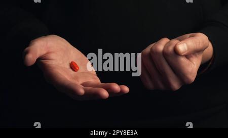 Studiofoto männliche Hände zeigen rote Pille isoliert auf schwarzem Hintergrund. Konzept der richtigen Wahl. Stockfoto
