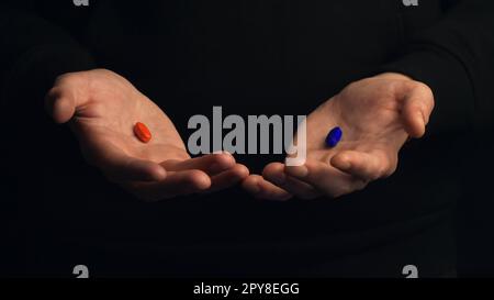 Studiofoto männliche Hände zeigen rote Pille und blaue Pille isoliert auf schwarzem Hintergrund. Konzept der richtigen Wahl. Stockfoto