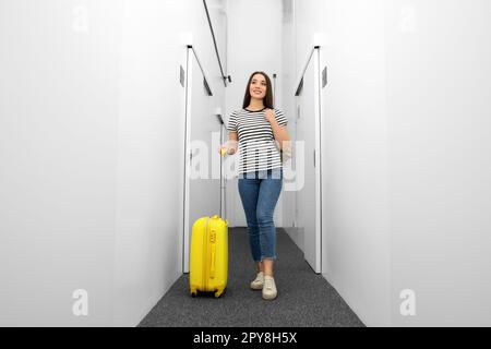 Glückliche junge Frau mit Rucksack und Koffer, die auf dem Korridor der Herberge spaziert Stockfoto