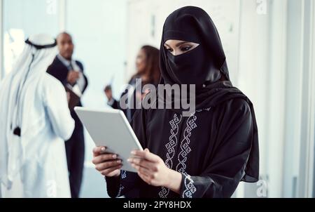 Effizient arbeiten, um die Arbeit zu erledigen. Eine attraktive junge arabische Geschäftsfrau, die mit ihren Kollegen im Büro an einem Tablet arbeitet Stockfoto